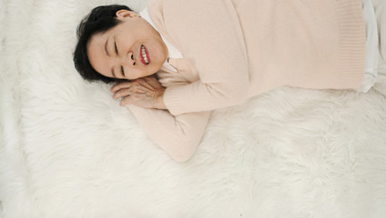 Obraz na płótnie Canvas Asian senior woman wear pink sweater sleep on white fur bed