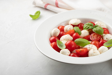 White plate of classic delicious caprese salad with ripe tomatoes, mozzarella and fresh basil leaves on gray background with copy space. Italian food. The concept of a healthy vegetarian diet