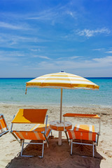Beach equipment, chairs and sun umbrella on white sandy beach with light blue sea water, beach vacation concept