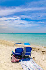 Beach equipment, chairs on white sandy beach with light blue sea water, beach vacation concept