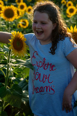 Beauty joyful young girl with sunflower enjoying nature and laughing on summer sunflower field. Sunflare, sunbeams, glow sun. Backlit.