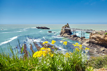 Biarritz city and view of its the famous landmark Rocher de la Vierge, a statue of Virgin Mary on the rock. Bay of Biscay, Atlantic coast, Basque country, France. Summer sunny day - obrazy, fototapety, plakaty