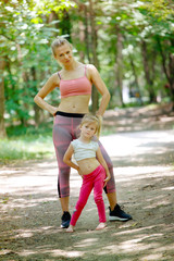 Woman and little girl posing in park after training. Family exercise, healthy lifestyle