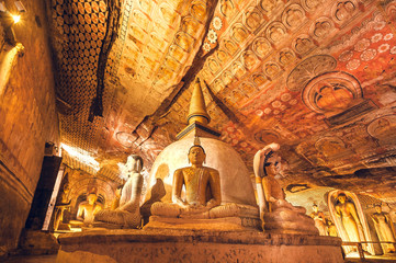 Colorful fresco on ceiling and sculptures of meditating Buddha in historical cave temple