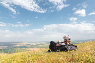 A professional paraglider in full gear and a helmet lies and rests on the grass high in the...
