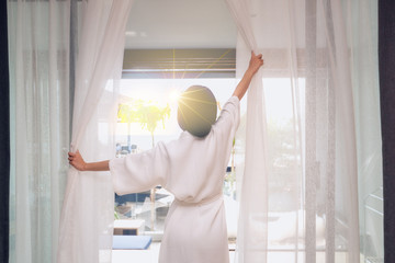 Woman open the curtain in the room looking to outside sea view. Women tourists staying in a hotel room at morning looking sunrise.
