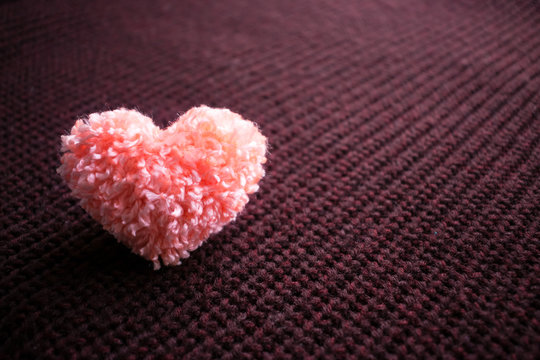 Fluffy pink thread heart on dark knitted burgundy background. Handmade pretty heart. Love, romance, Valentines day DIY concept. Selective focus