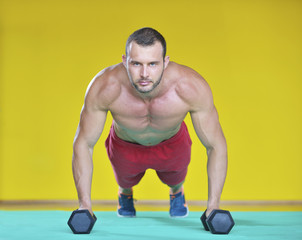 Obraz premium Strong attractive man performs exercises using a resistance band. Photo of muscular male isolated on yellow background. Strength and motivation