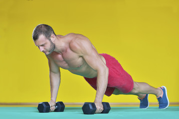 Strong attractive man performs exercises using a resistance band. Photo of muscular male isolated on yellow background. Strength and motivation