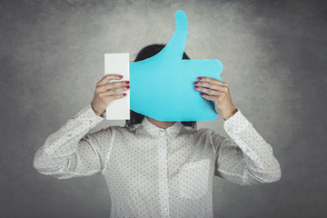 Young Woman holding a like icon on gray background - obrazy, fototapety, plakaty