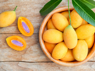 Marian plum or mayongchid fruit with green leaf in wooden bowl on the  table in topview.