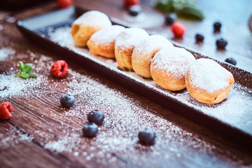 Donuts sprinkled with powdered sugar on a black long plate with raspberry bilberry and mint.