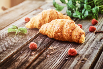 Croissants decorated with raspberries and mint on a wooden boards.
