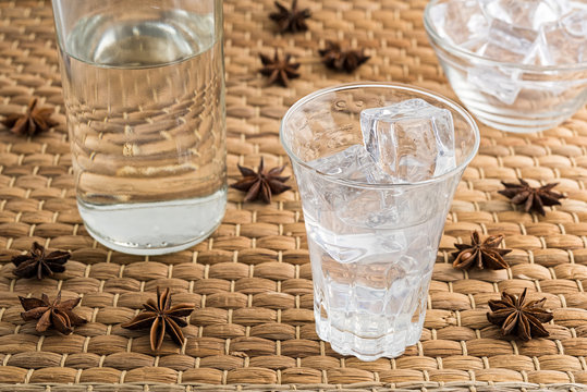 Glass and bottle of traditional drink Ouzo or Raki with anise star seeds on natural matting
