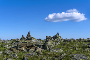 bright landscape of a high-altitude plateau with folded travelers pyramids cairns of stones under a blue sky with clouds..