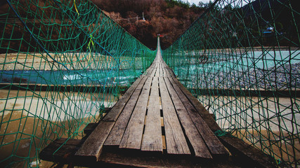 Old wooden suspension bridge over the mountain river close up.