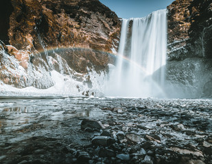 Skogafoss waterfall in Iceland with rainbow on a sunny day with blue sky.