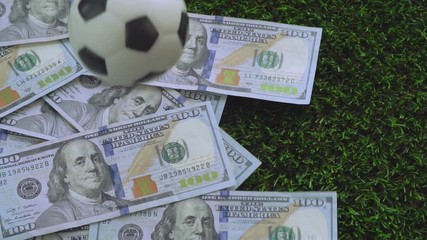Football business, soccer gambling concept : A football dropping on US dollar bills, which spread over green grass. Slow motion VDO. - Powered by Adobe