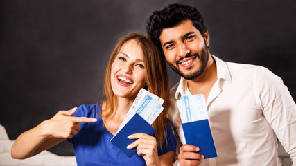 Young happy couple of travelers with tickets and passports smiling indoors on the world map background