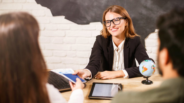 Beautiful female travel agent in glasses is working with clients in office and offering them tours