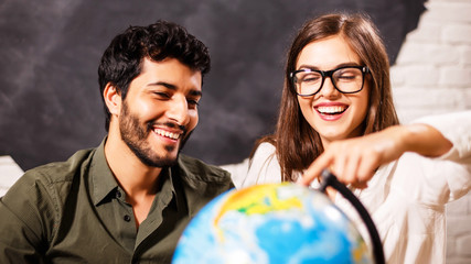 Excited young couple planning their holiday holding up a globe and pointing to a travel destination