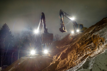 The yellow excavator works at night in the headlights and additional lights. Loads of sand. Night shooting.