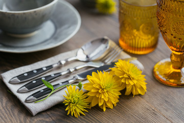 Rustic table setting with linen napkin, cutlery, ceramic plates, yellow glasses and yellow flowers