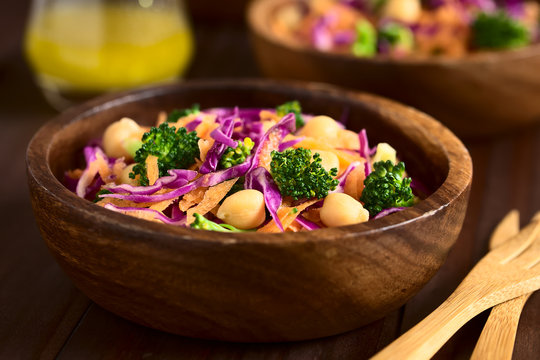 Frischer Salat aus Rotkohl, Kichererbsen, Karotten und Broccoli serviert in Holzschüsseln, fotografiert mit natürlichem Licht (Selektiver Fokus, Fokus in die Mitte des Bildes)