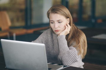 Thoughtful concept. Woman working on a computer at a cafe while gazing through the window glass.