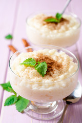 Rice pudding with cinnamon and mint on light purple wooden background