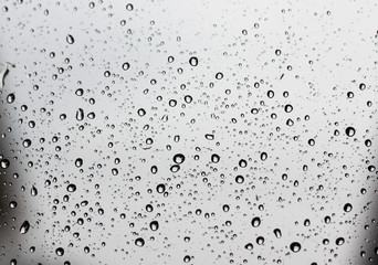 Pure raindrops on a window glass surface on a gray clouds background. Water drops pattern close up...