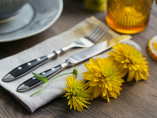 Rustic table setting with linen napkin, cutlery, ceramic plates, yellow glasses and yellow flowers