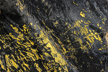 Abstract black burnt rubber background with yellow peeling paints. Dirty scratched burn elastic gum with orange dye peels