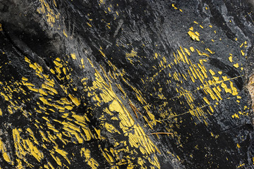 Abstract black burnt rubber background with yellow peeling paints. Dirty scratched burn elastic gum with orange dye peels