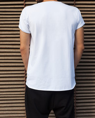 Fashion street youth. A man in a white T-shirt posing with his back to the camera on a dark blue...