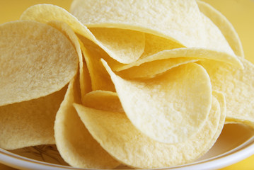 Many potato chips in round plate isolated on yellow background. Snack food.