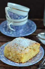 Piece of apple pie sprinkled with powdered sugar on a wooden background