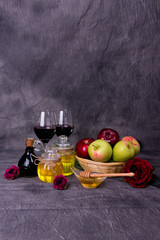 Rosh Hashanah Jewish holiday concept - Green and red apples in basket, dipper in saucer of honey, two Honey jars, red flowers, glasses of red wine and vintage bottle of wine
