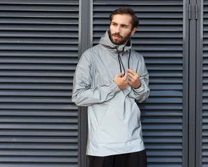 Modern materials in the fashion industry. Windbreaker from the rain. A man is posing in a fashionable silvery waterproof jacket made of new technological materials.
