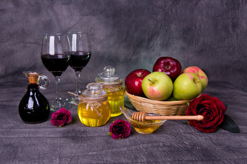 Rosh Hashanah Jewish holiday concept - Green and red apples in basket, dipper in saucer of honey, two Honey jars, red flowers, glasses of red wine and vintage bottle of wine