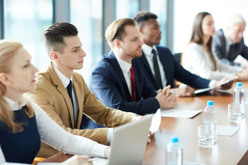 Serious business people in formalwear concentrated on information watching presentation and listening to speaker at conference