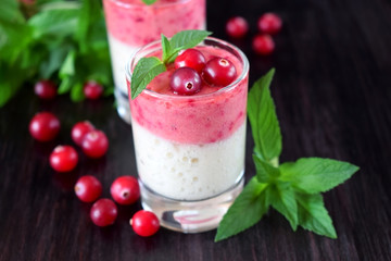 Two layered smoothie in glasses surrounded by cranberries and mint against the dark background