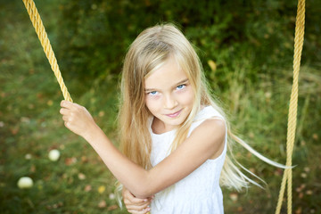A child cute girl swinging on a rope ladder in summer in the garden