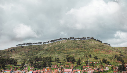 Fototapeta na wymiar Trees line a lush green hilltop over a small town in Bolivia