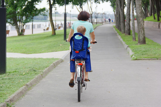 A Woman Is Rolling A Bicycle With A Child Seat.