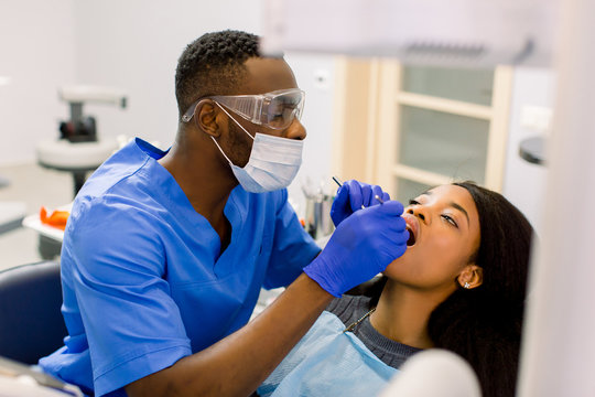 Male african dentist examining a patient with tools in dental clinic. African female patient getting dental treatment in dental clinic