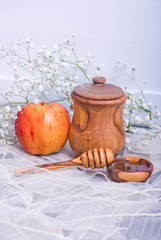 Rosh Hashanah Jewish holiday concept - red yellow apple, wooden dipper, saucer of honey and Honey jar on white leaves table and white flowers. Traditional holiday symbols