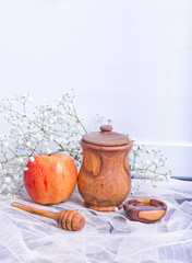 Rosh Hashanah Jewish holiday concept - red yellow apple, wooden dipper, saucer of honey and Honey jar on white leaves table and white flowers. Traditional holiday symbols