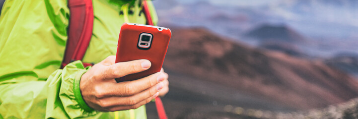 Mobile phone man using his cellphone texting a text message during hiking travel abroad in nature mountains, banner panorama.