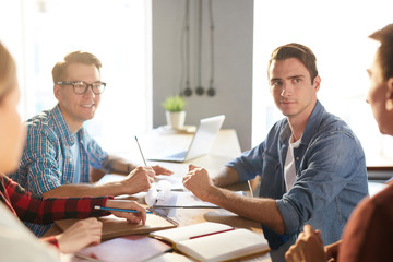 Group of young business professionals discussing ideas while collaborating on startup project during meeting in modern office, focus on handsome man listening to colleagues